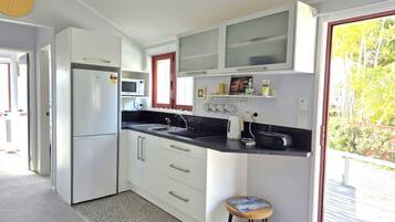 A compact kitchen with white cabinets, a microwave, a sink, and a small stool.