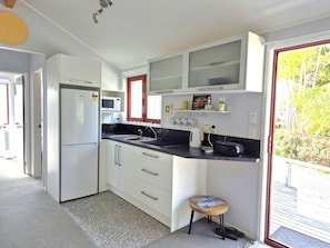 A compact kitchen with white cabinets, a microwave, a sink, and a small stool.