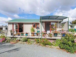 A two-story house with a covered porch, a green roof, and a variety of potted plants and flowers.