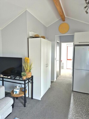 A compact living space with a kitchenette, a sofa, a TV, and a hallway leading to another room.