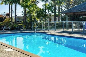 A clear swimming pool with a metal fence, surrounded by palm trees and a covered area.