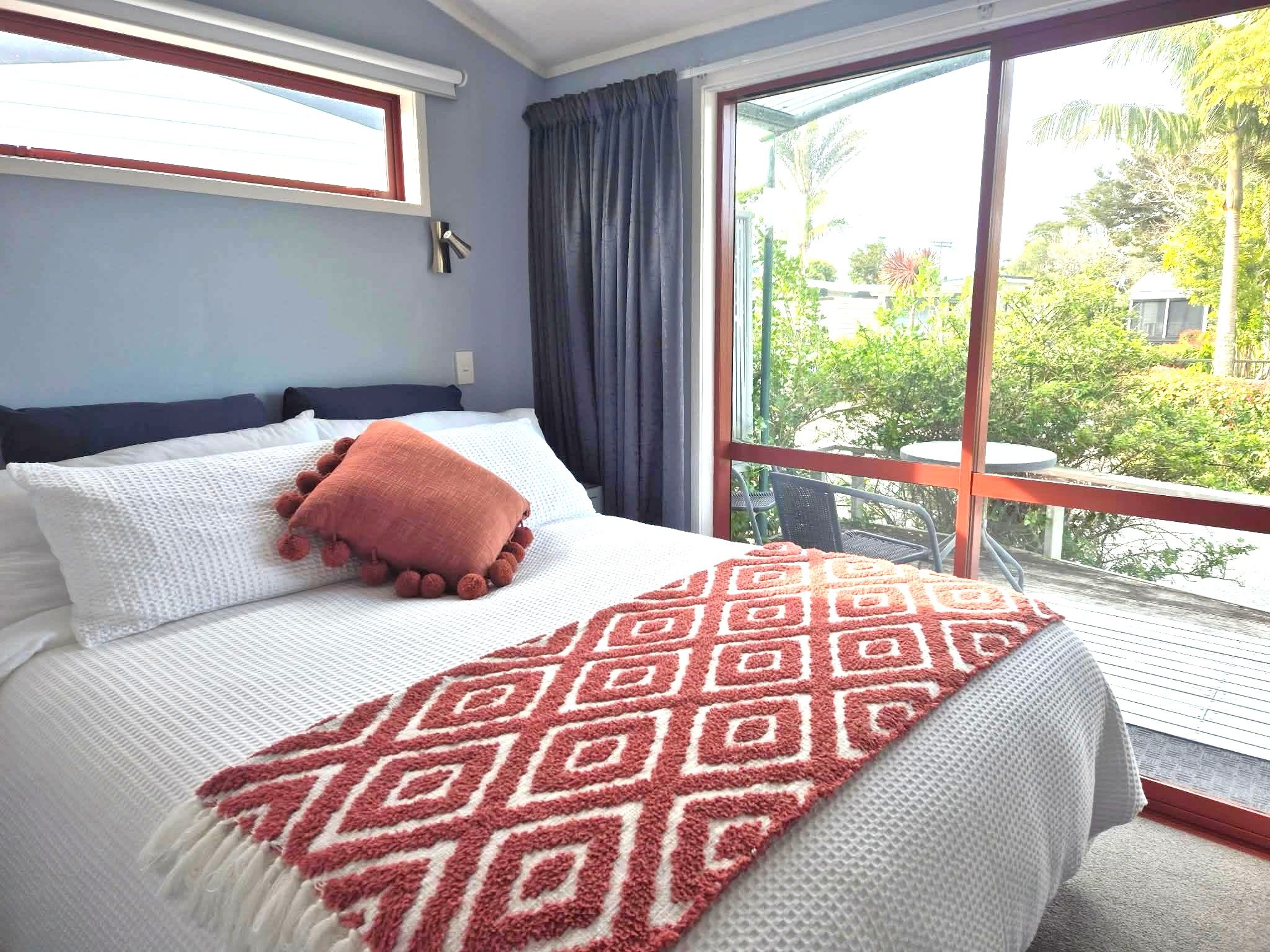 A bedroom with a large bed, a window with curtains, and a view of greenery outside.