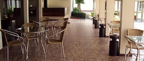Un patio al aire libre con mobiliario de mimbre, piso de baldosas y vistas al exterior.