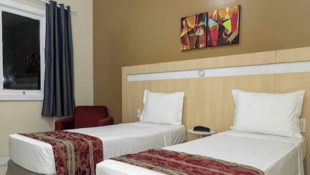 A hotel room with two single beds, a red chair, a small table, and a window with curtains. - Welcoming Room Perfect for Quick Weekend Escape Near Parque da Cidade - 1.3 mile (Pará)