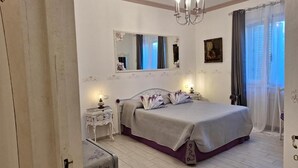 Un dormitorio con cama, mesita de noche, espejo, candelabro y cortinas.