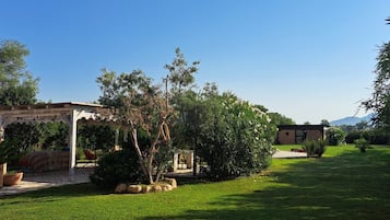 Un jardí amb una pèrgola, un edifici petit i una zona enjardinada.
