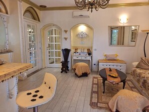 A room with a dining table, a chair, a sofa, a small table with a lamp, and a mirror on the wall.