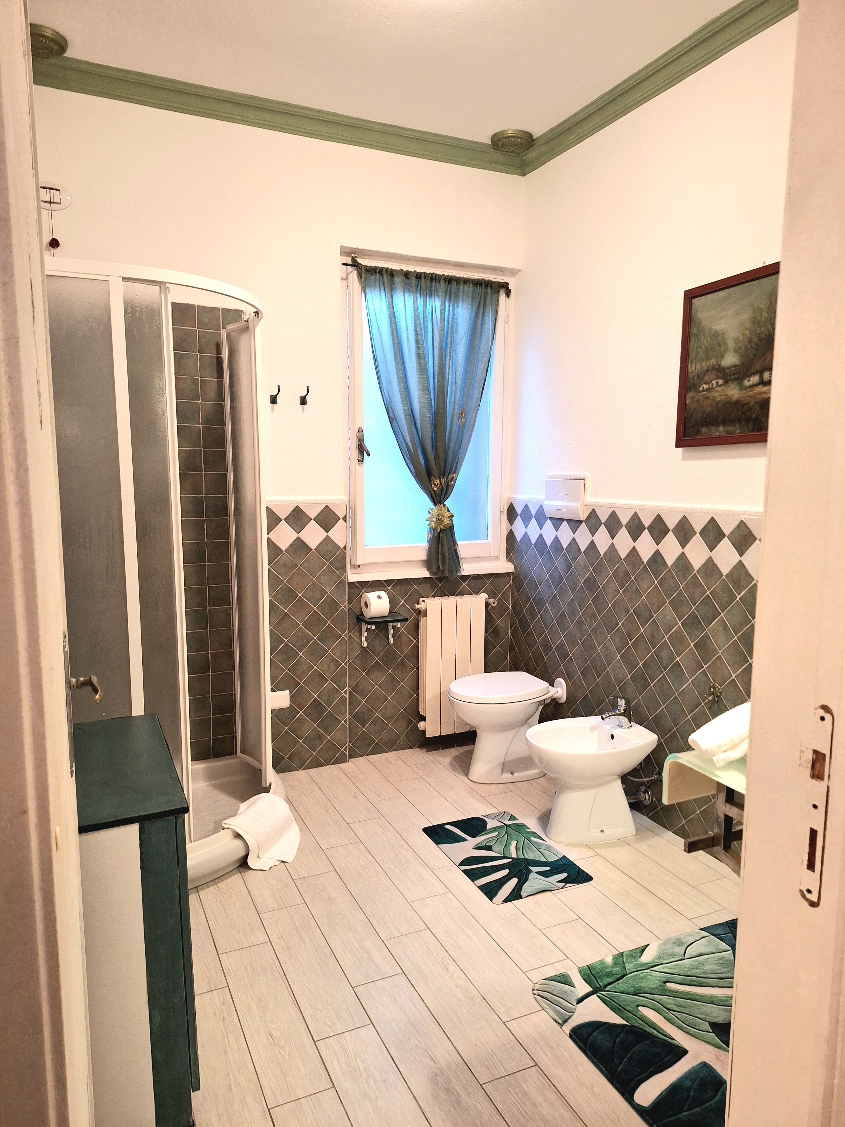 Un baño con ducha, inodoro, bidé y ventana con cortina.