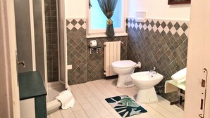 Un baño con ducha, inodoro, bidé y ventana con cortina.