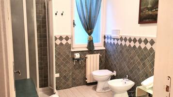 Un baño con ducha, inodoro, bidé y ventana con cortina.