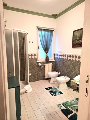 Een badkamer met een douche, toilet, bidet en een raam met gordijn.