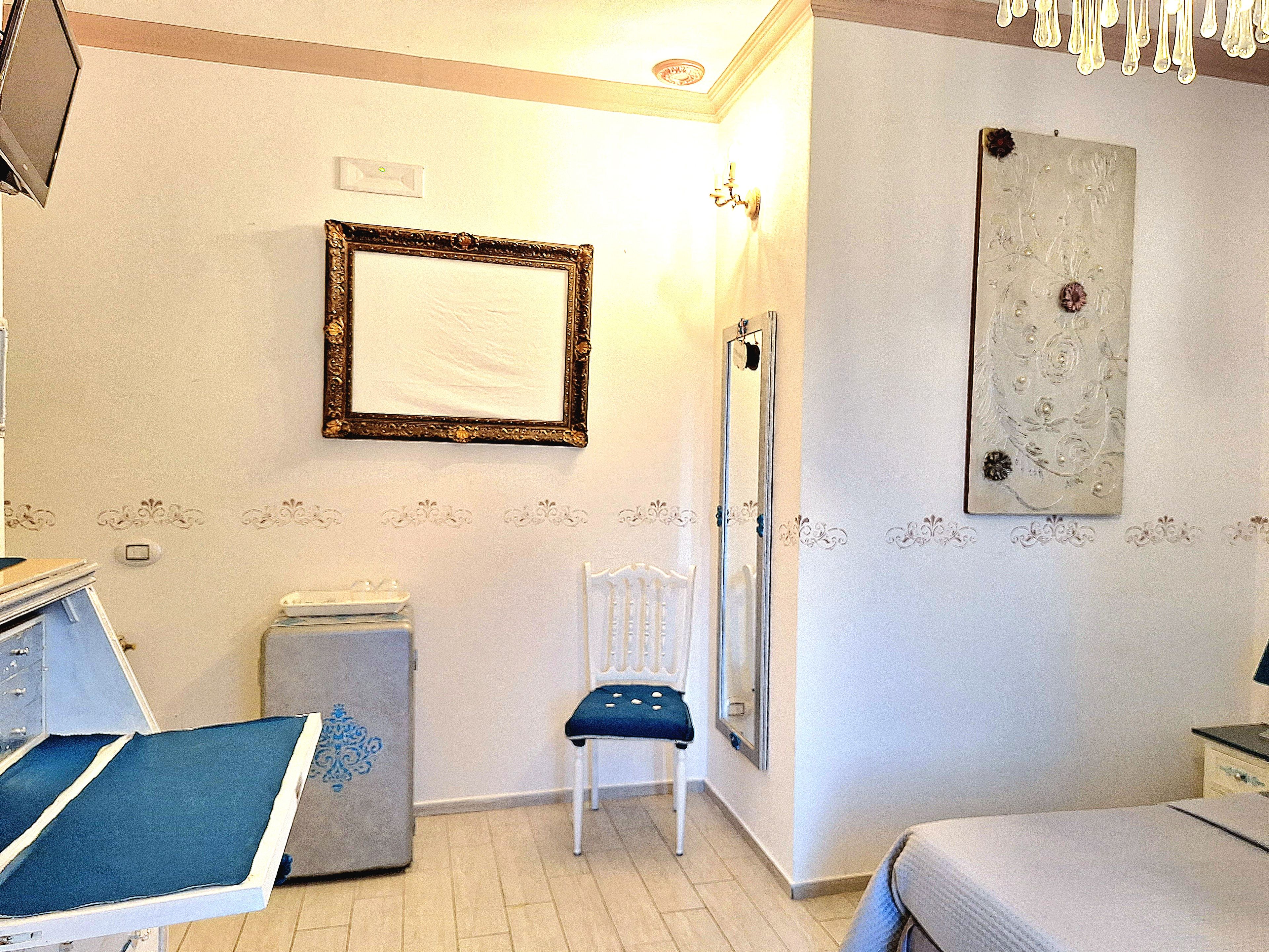 Una habitación con cama, una silla, un escritorio con computadora, un espejo y una pared con detalles decorativos.