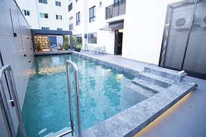 Una piscina interior moderna con agua cristalina, escalones para entrar y una zona de estar con sillas y una mesa.