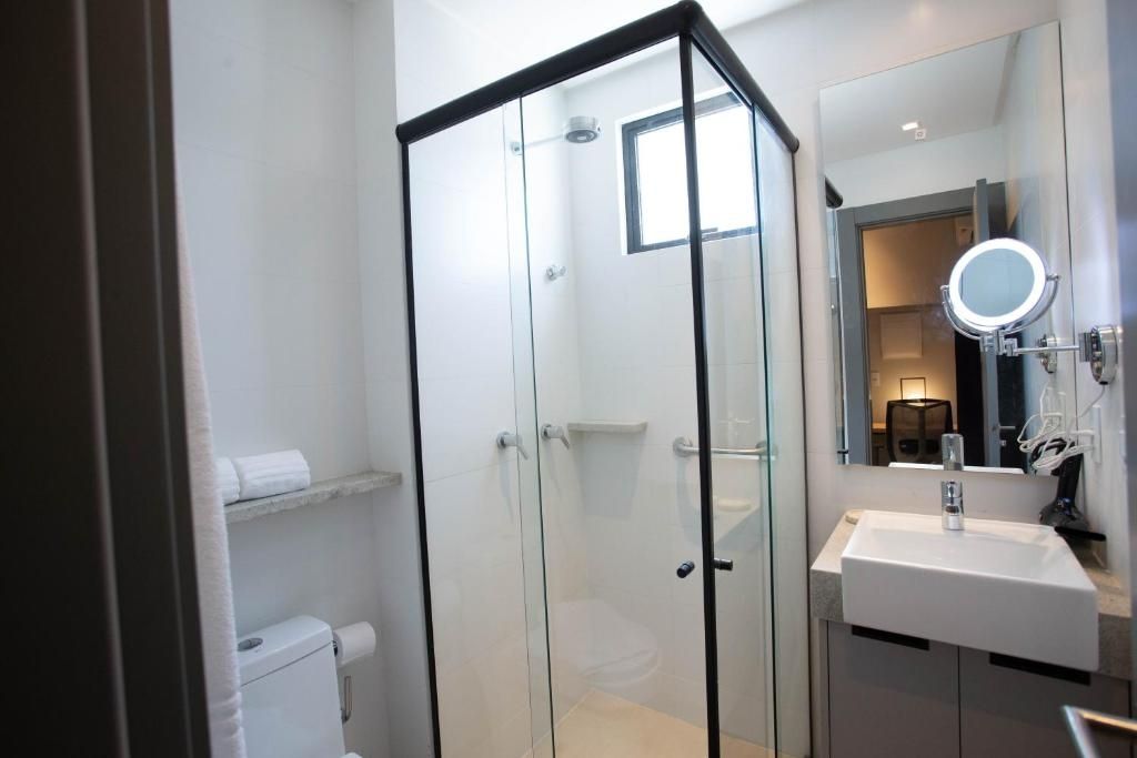 A modern bathroom with a glass-enclosed shower, a white sink, and a mirror with a round mirror above it.