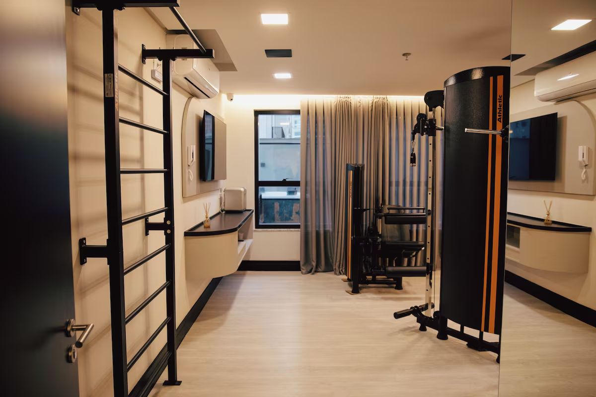 Une chambre d’hôtel moderne dotée d’un espace d’entraînement, comprenant une barre de traction, un appareil d’exercice et un grand objet cylindrique noir.