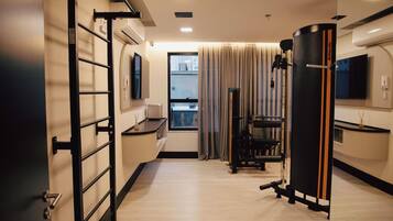 Une chambre d’hôtel moderne dotée d’un espace d’entraînement, comprenant une barre de traction, un appareil d’exercice et un grand objet cylindrique noir.
