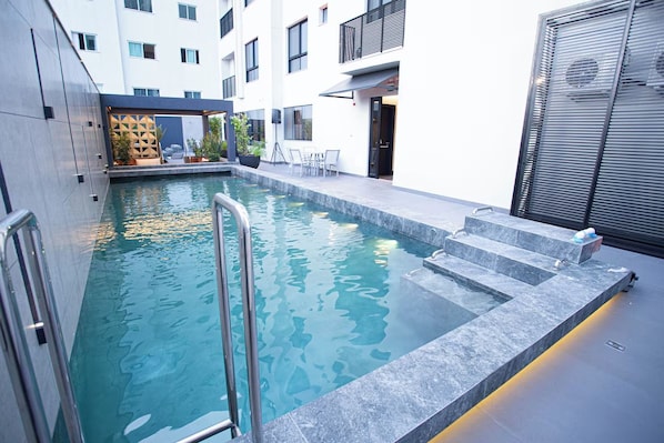 Una piscina interior moderna con agua cristalina, escalones para entrar y una zona de estar con sillas y una mesa.