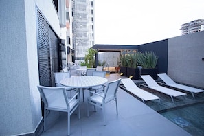 Una terraza en la azotea con piscina, sillones de descanso y una mesa con sillas.