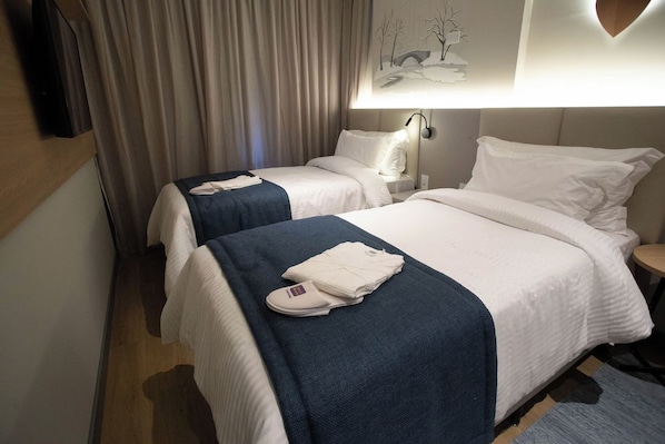 Ein Hotelzimmer mit zwei Betten, einem Flachbildfernseher, einer Wandlampe und einem Gemälde.