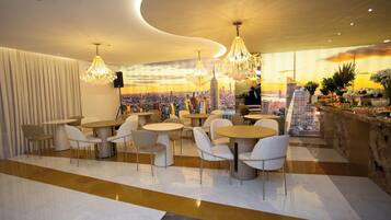 Un restaurant moderne avec des tables et des chaises rondes, une fresque représentant un paysage urbain sur le mur et une vue sur les bâtiments de la ville.
