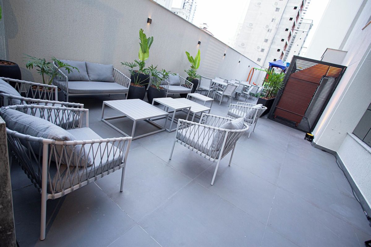 Uma área de pátio ao ar livre com móveis de vime, plantas em vasos e vista para a cidade.