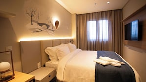 Ein Hotelzimmer mit Bett, Schreibtisch, Flachbildfernseher und Wandbild.