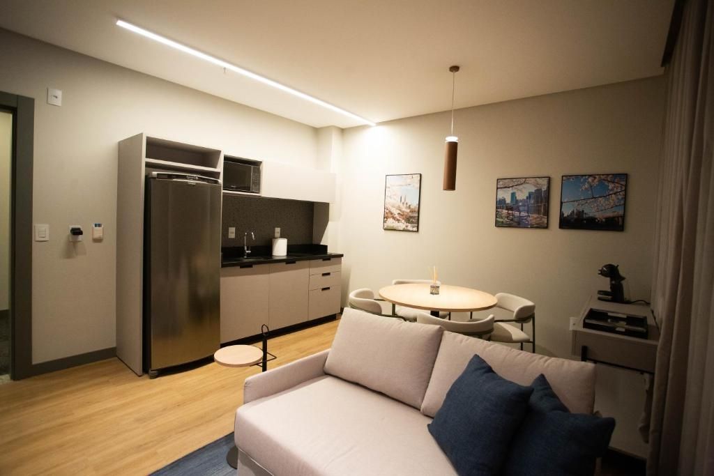 Um espaço de estar moderno com uma kitchenette, uma mesa de jantar redonda e um sofá com almofadas.