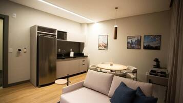 Um espaço de estar moderno com uma kitchenette, uma mesa de jantar redonda e um sofá com almofadas.