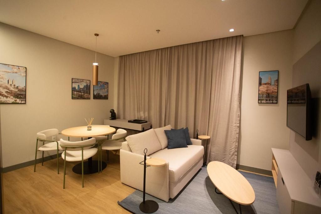 Una habitación de hotel moderna con sofá, mesa de comedor, sillas, televisor y obras de arte en las paredes.