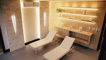 Une salle de spa moderne avec deux fauteuils blancs, un comptoir d’accueil en bois doté d’étagères et un climatiseur fixé au mur.