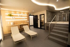 Moderni hotellin aula, jossa on kaksi nojatuolia, vastaanottotiski, portaikko ja spa-alue.