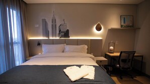 A hotel room with a large bed, a desk, and a chair. There is a painting of buildings on the wall and a lamp on the desk. - Ocean Room with Full Kitchen Perfect for Family Getaways Near Itapema Beach (Santa Catarina)