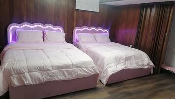 Une chambre avec deux lits, des murs en bois, un luminaire au plafond et une fenêtre avec des stores.