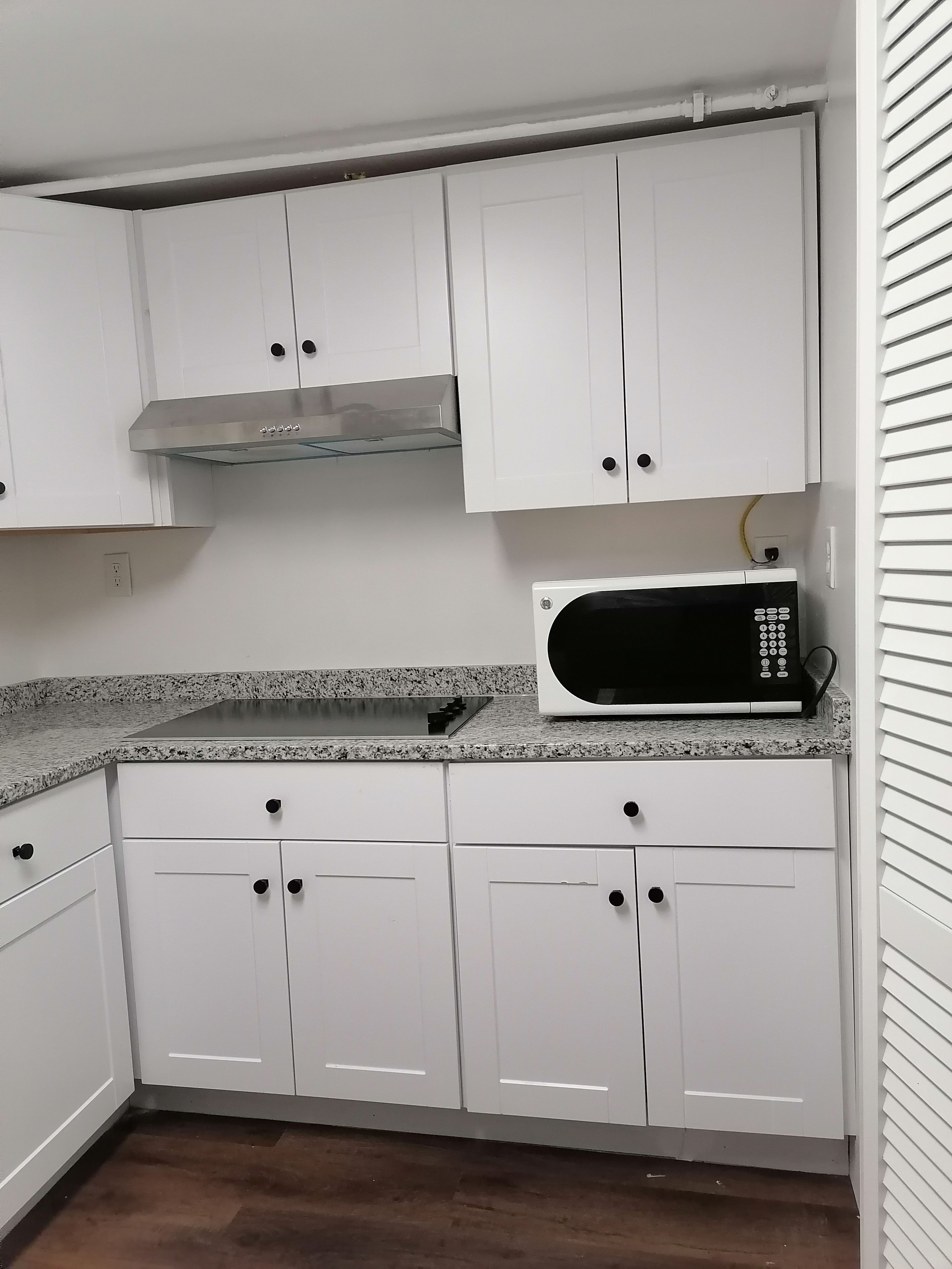 Una cocina con gabinetes blancos, una campana extractora de acero inoxidable, un microondas y una encimera de granito.