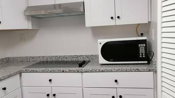 Una cocina con gabinetes blancos, una campana extractora de acero inoxidable, un microondas y una encimera de granito.