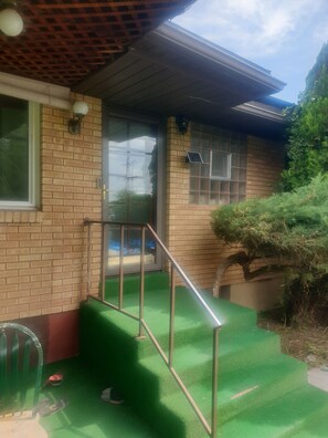A brick building with a green artificial turf step leading to a door, a window with a metal grill, and a solar panel on the wall.