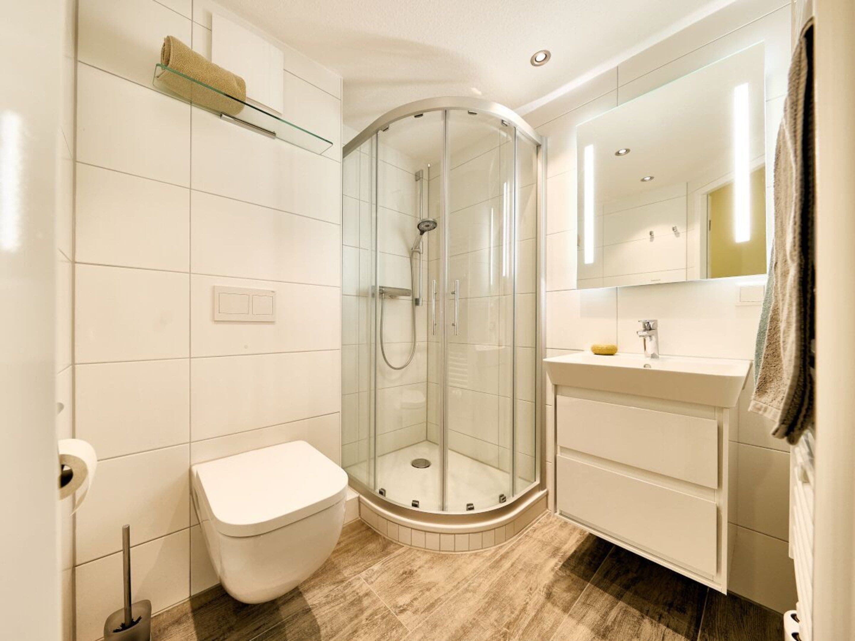 A modern bathroom with a glass-enclosed shower, a white toilet, and a vanity with a mirror.
