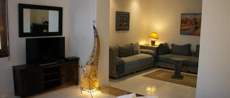 Uma sala de estar com um sofá, uma televisão, um abajur e uma luminária decorativa.
