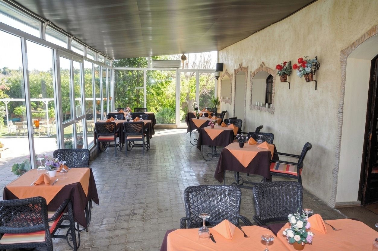 Un'area pranzo all'aperto con tavoli e sedie, ampie finestre e vista sul verde.