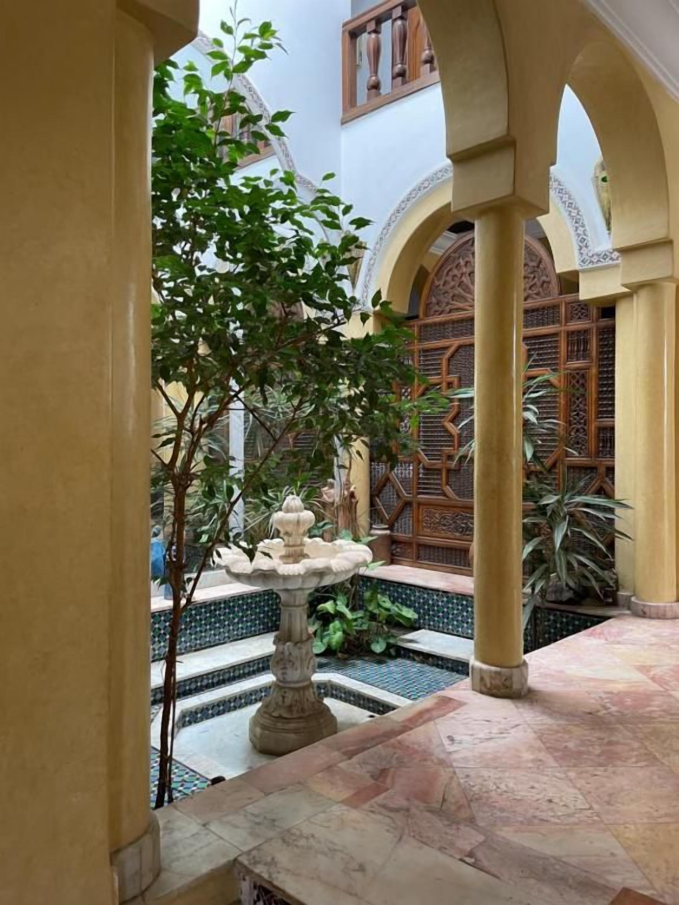 A courtyard with a fountain, tiled floor, and a wooden gate.