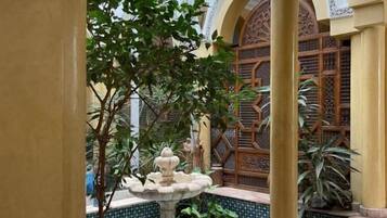 A courtyard with a fountain, tiled floor, and a wooden gate.