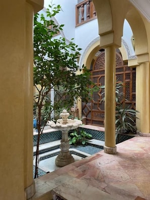 A courtyard with a fountain, tiled floor, and a wooden gate. - Gite Nadia (Oulad Azzouz)