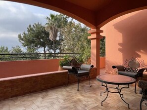 Un patio exterior con una mesa redonda y dos sillas, un muro de ladrillo y vistas a árboles.