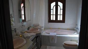 Een badkamer met een badkuip, twee wasbakken, een toilet en een grote spiegel.