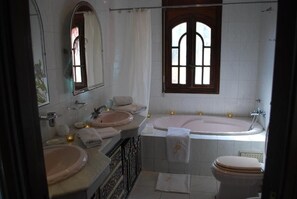 Un baño con bañera, dos lavamanos, inodoro y un espejo grande.