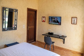A hotel room with a bed, a desk, a chair, a television, and a door. - Gite Nadia (Oulad Azzouz)