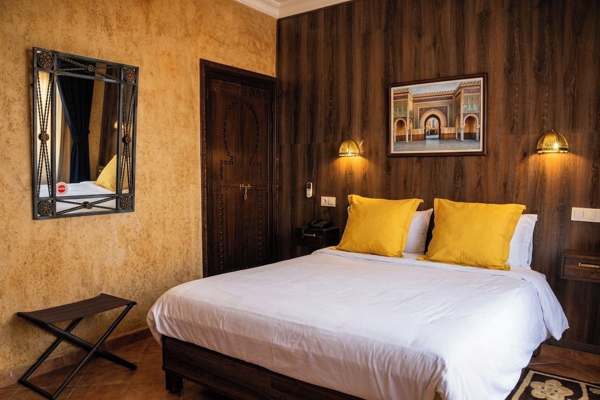 A hotel room with a bed, a wooden door, a mirror, and a wall-mounted picture.