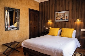 Habitación de hotel con una cama, una puerta de madera, un espejo y un cuadro colgado en la pared.