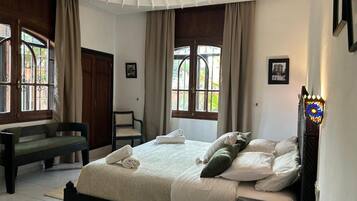 A bedroom with a bed, a bench, and a window with curtains.