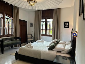 A bedroom with a bed, a bench, and a window with curtains. - Gite Nadia (Oulad Azzouz)